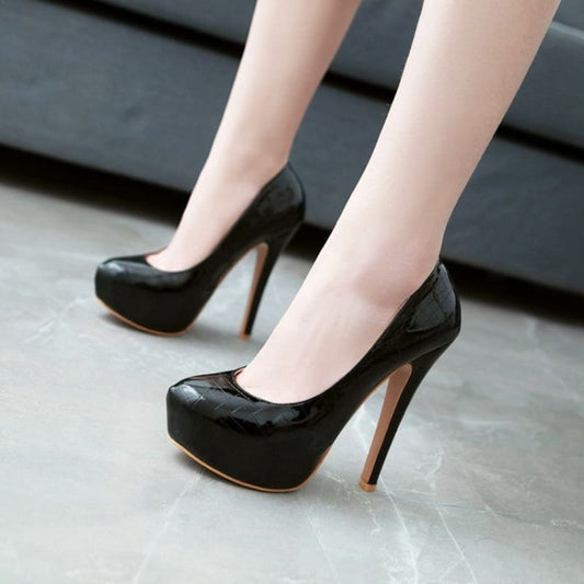 Pair of glossy black high-heeled platform pumps worn on pale legs.